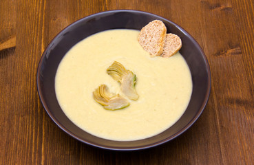Cream of artichokes and croutons on wooden table