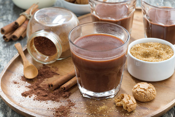 glass of cocoa with spices and cookies on a wooden tray