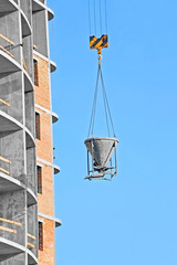 Crane lifting concrete mixer container against blue sky