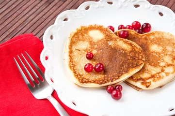 Heart shaped pancakes with cranberries on porcelain plate. Close