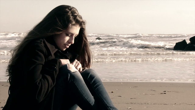 Girl on the beach sitting depressed in the winter