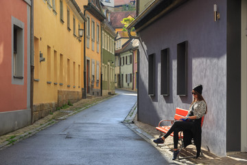 Teenage girl sitting on the bench on old city street