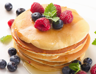 Sweet pancakes with raspberries and blueberies on a  white plate