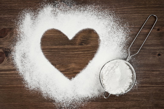 Heart shape of flour on brown wooden board background