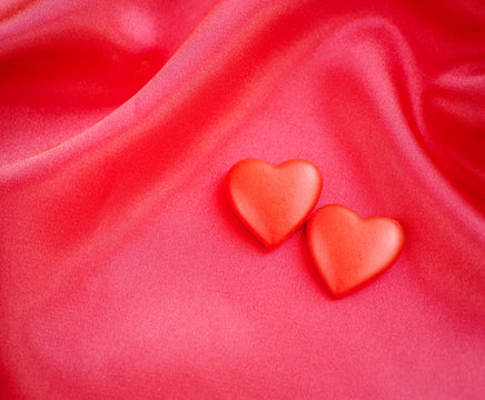 Two red hearts on satin fabric background
