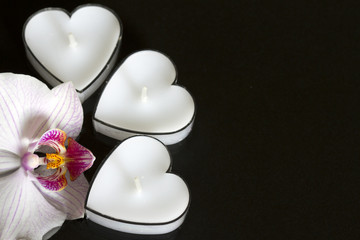 Fototapeta na wymiar Candles hearts with orchid on black background love concept