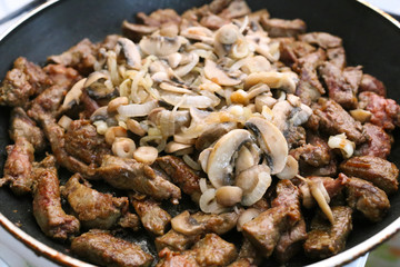 beef liver bits with champignons and onion on a pan