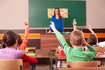 Children in elementary school are raised hand in classroom