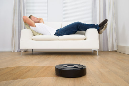 Robotic Vacuum Cleaner In Front Of Man Relaxing