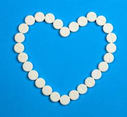 White round pills in heart shaped on blue background