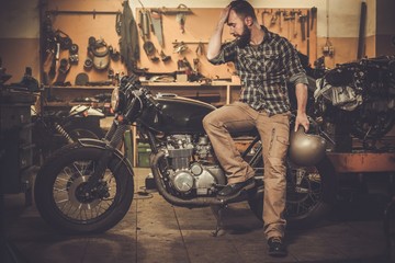 Naklejka premium Man and vintage style cafe-racer motorcycle in garage