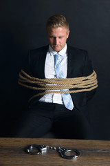 Businessman Tied With Rope Sitting In Front Of Table