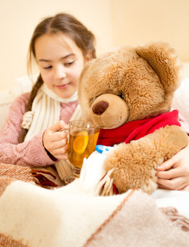 sick girl lying in bed and giving tea to teddy bear