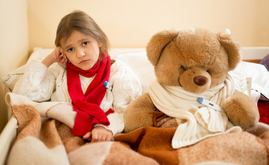 sad girl measuring temperature with teddy bear in bed