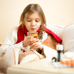 little sick girl lying in bed and blowing on hot tea