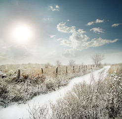 Snow-covered road past the fence in a field