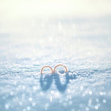 Wedding concept - close up two gold rings on the snow in winter sunny day