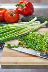 Chopped green onions and vegetables on striped wooden board