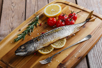 Baked mackerel with tomato and lemon on wooden board