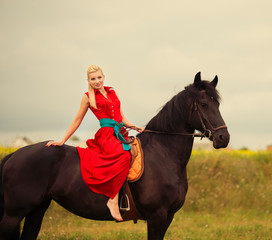 Obraz premium Fashionable blonde woman riding a horse in sunny day. Long hair.