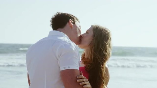 perfect kiss - romantic couple kissing at beach with ocean waves and breeze - man and woman in love 4K and 1080 HD