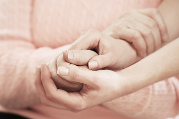 Old and young holding hands on light background, closeup