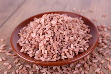 Red rice on plate on wooden background
