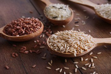 Different kinds of rice in spoons on wooden background
