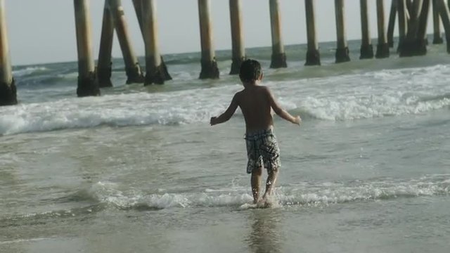 child playing at beach - boy having fun with ocean waves in slow motion 4K and 1080 HD