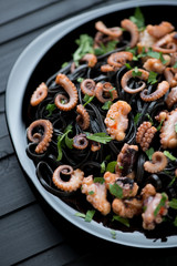 Squid ink coloured tagliatelle with sliced octopus, close-up