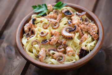 Tagliatelle with octopuses in a ceramic bowl, wooden background