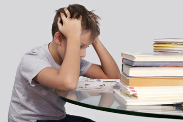 Мальчик сидит за столом в окружении книг взявшись за голову