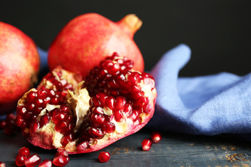 Juicy ripe pomegranates on wooden table, on dark background