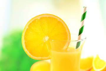 Glass of orange juice with straw and slices on bright