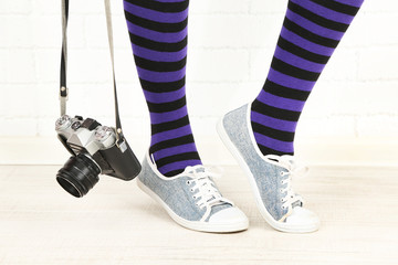 Girl in sneakers with retro photo camera in room