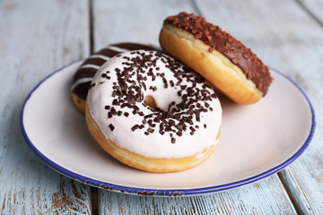 Delicious donuts with icing on plate on wooden background