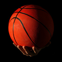 Male hands holding basketball ball on dark background