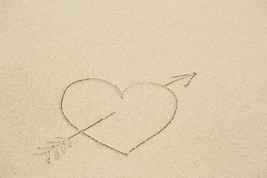 Picture of a heart pierced with an arrow on wet beach sand