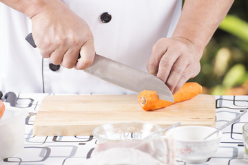 Chef cutting carrot on wooden broad
