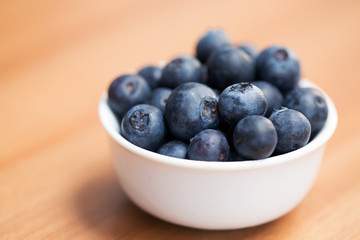 A white bowl with ripe blueberries on a table, shallow dof