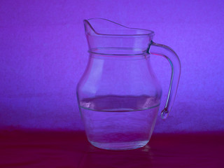 Glass jug with water on purple, mauve background.