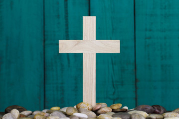 Wood cross in stones by teal blue rustic wooden background