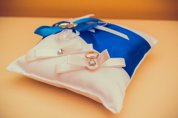 Two gold wedding rings lying on white with blue pillow