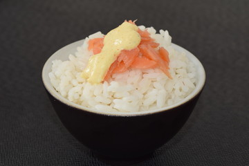 Sushi with salmon and sauce in a bowl on a black background.
