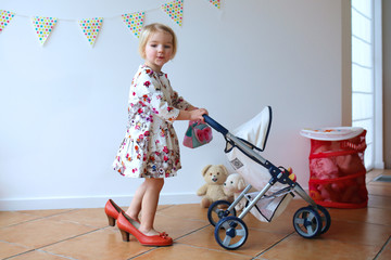 Little girl playing mom's-to-be role walking with pram and doll