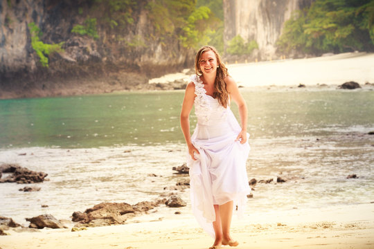 young blonde bride walks barefoot on sandy beach