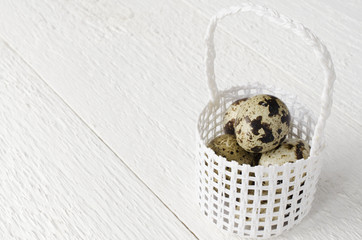 Quail eggs in a white wicker basket on a white wooden table, tex