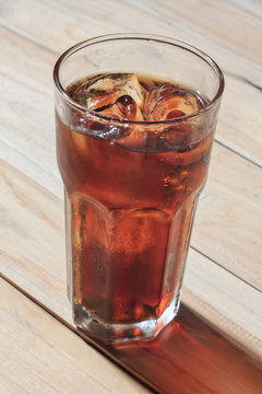 glass of cola with ice on wood