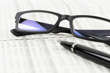 Pen and glasses rest on stock price detail financial newspaper