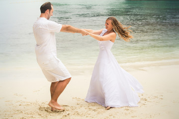 Fototapeta na wymiar blonde bride and groom dance standing at sand beach